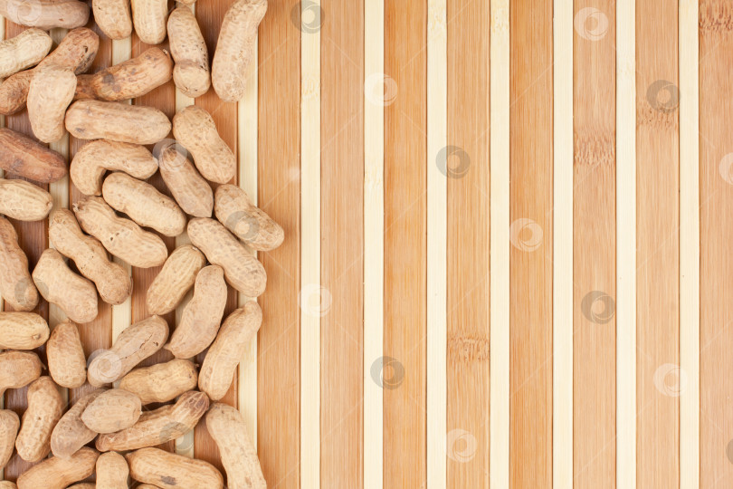 Скачать В качестве фона можно использовать неочищенный арахис, лежащий на бамбуковой циновке. unpeeled peanuts lying on a bamboo mat can be used as background фотосток Ozero