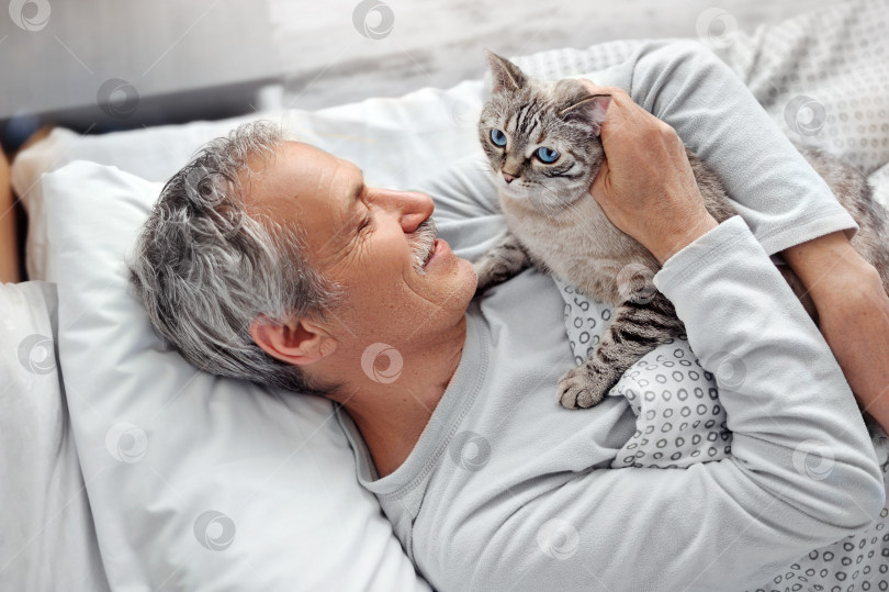 Скачать Пожилой мужчина обнимает кошку в постели фотосток Ozero
