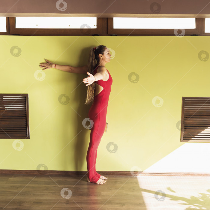 Скачать Женщина, практикующая йогу, выполняет упражнение на растяжку мышц грудной клетки у стены, тренируется стоя в студии фотосток Ozero