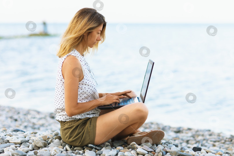 Скачать Женщина работает за компьютером на берегу моря, совмещает отдых и работу фотосток Ozero