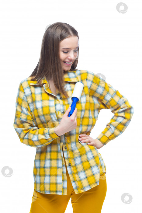 Скачать Портрет молодой женщины, использующей средство для удаления ворса, чтобы очистить желтую клетчатую рубашку от пыли, волос, ворса и пуха, выделенный на белом фоне фотосток Ozero