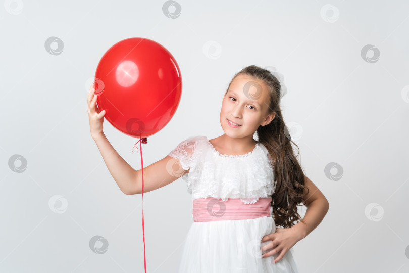 Скачать Портрет счастливой девушки в белом платье, держащей в руке один красный воздушный шарик, улыбающейся и смотрящей в камеру фотосток Ozero