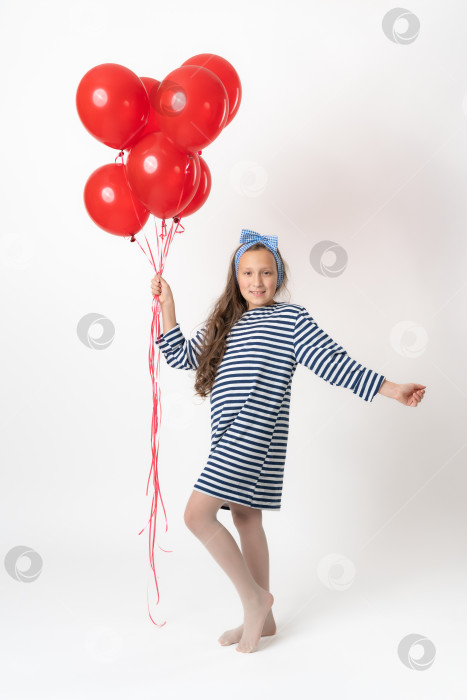 Скачать Девушка держит в руке связку красных воздушных шаров, смотрит в камеру. Модель в полный рост на белом фоне фотосток Ozero