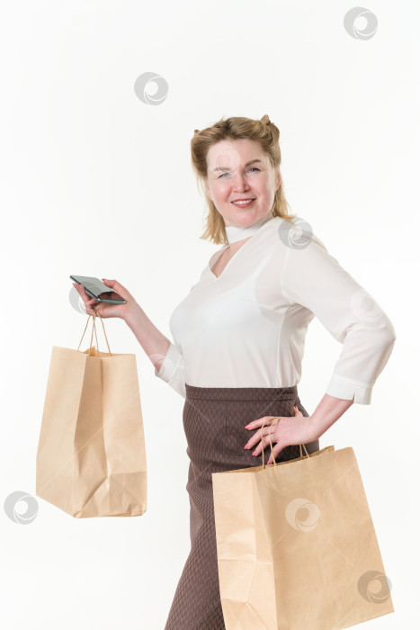 Скачать Зрелая женщина держит в руках одноразовые бумажные пакеты с покупками после похода по магазинам, используя мобильный телефон фотосток Ozero