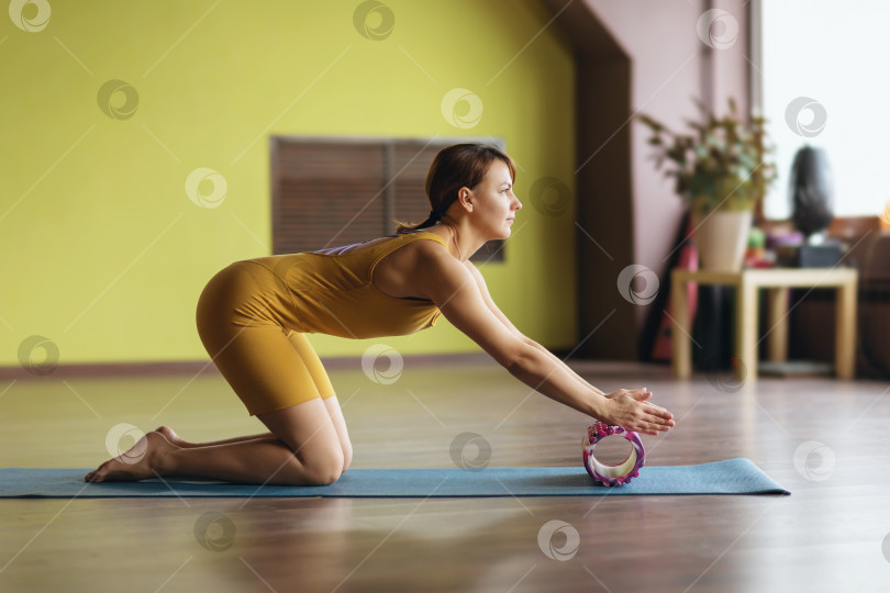 Скачать Женщина в спортивной одежде выполняет миофасциальный массаж мышц ладоней и предплечий с помощью валика, тренируется на коврике в комнате фотосток Ozero