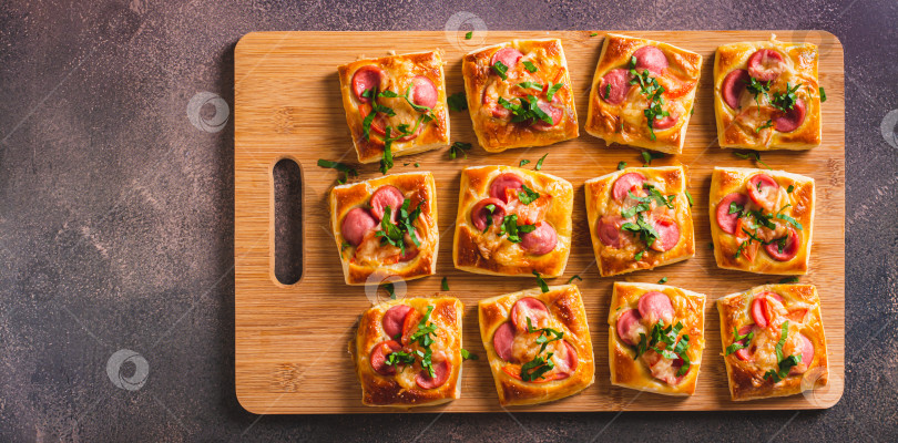 Скачать Закусочная мини-пицца с сосисками, помидорами и сыром на деревянной доске вид сверху веб-баннер фотосток Ozero