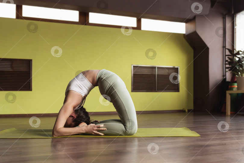 Скачать Женщина, практикующая йогу, выполняет упражнение Капотасана, позу голубя, тренируется в студии на коврике фотосток Ozero