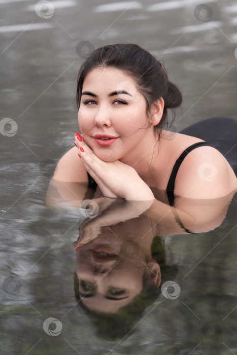 Скачать Молодая женщина увеличенных размеров в черном купальном костюме лежит в минеральной воде в открытом бассейне спа-центра фотосток Ozero