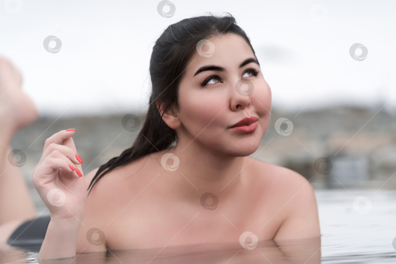 Скачать Счастливая молодая женщина больших размеров лежит и расслабляется в воде открытого бассейна в геотермальном спа-центре фотосток Ozero