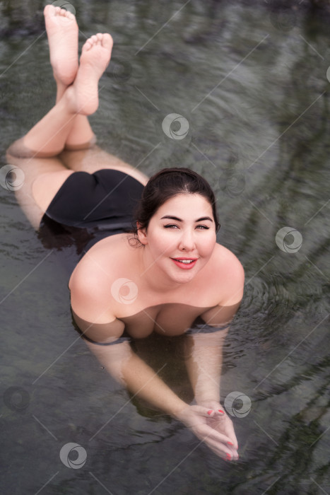 Скачать Модель с полной фигурой в черном купальном костюме, лежащая в геотермальной воде в открытом бассейне спа-центра фотосток Ozero