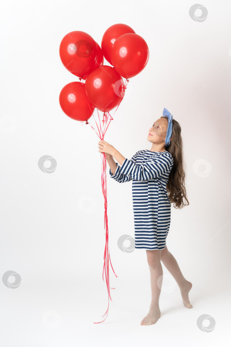 Скачать Любопытная девушка держит в двух руках связку красных воздушных шаров и смотрит на воздушные шары на белом фоне фотосток Ozero