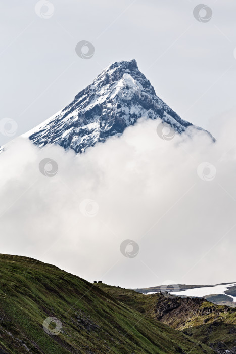 Скачать Красивый горный пейзаж, вид на заснеженную вершину скалистого конуса вулкана в облаках фотосток Ozero