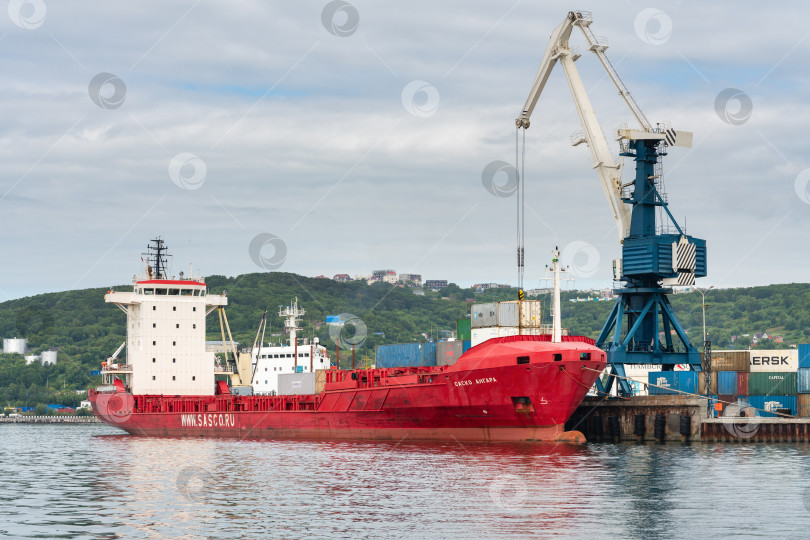 Скачать Портальный кран разгружает грузовой контейнеровоз Sasco Angara Российского Сахалинского морского пароходства на причале контейнерного терминала морского порта фотосток Ozero