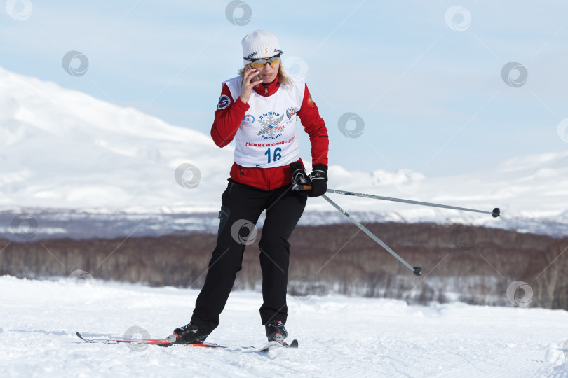 Скачать Спортсменка-лыжница бежит по зимней лыжне и разговаривает по смартфону фотосток Ozero
