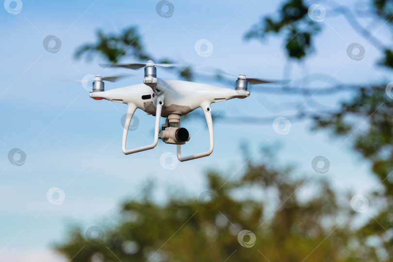 Скачать Беспилотный квадрокоптер DJI Phantom летит в летнем голубом небе и делает снимки фотосток Ozero