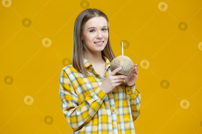 Скачать Портрет красивой молодой улыбающейся женщины, держащей в обеих руках кокосовый орех с соломинкой, выделенной на желтом фоне. Концепция здорового образа жизни, правильное питание, диета, веган, вегетарианец фотосток Ozero