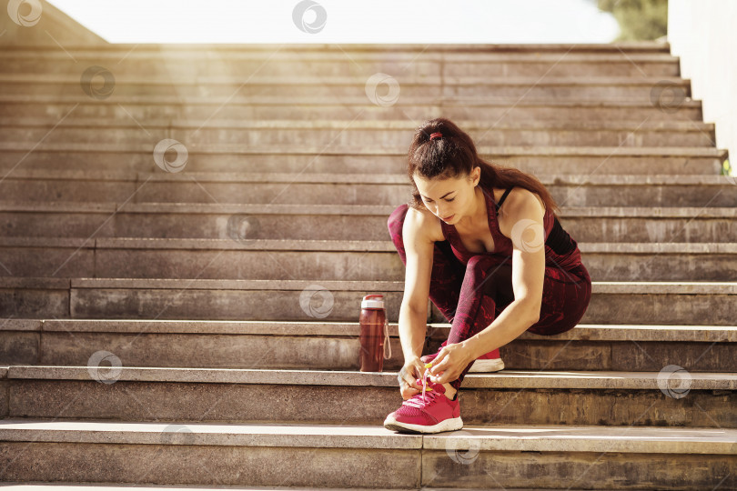 Скачать Женщина-спортсменка завязывает шнурки на кроссовках, сидя на подоконнике фотосток Ozero