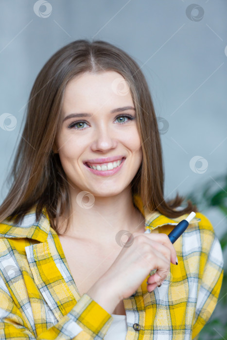 Скачать Крупным планом фотография улыбающейся смеющейся молодой женщины, смотрящей в камеру и держащей синюю электронную сигарету фотосток Ozero