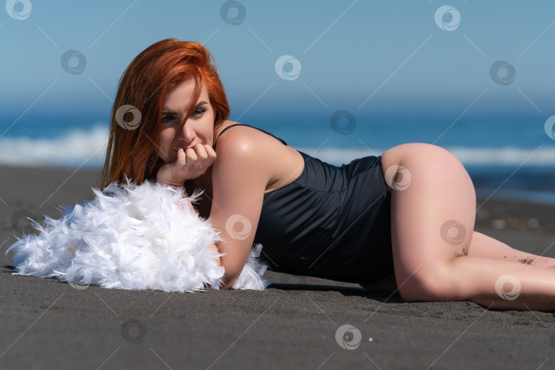 Скачать Женщина лежит на песчаном пляже в черном купальнике, подпирает подбородок рукой, смотрит в сторону и загорает фотосток Ozero