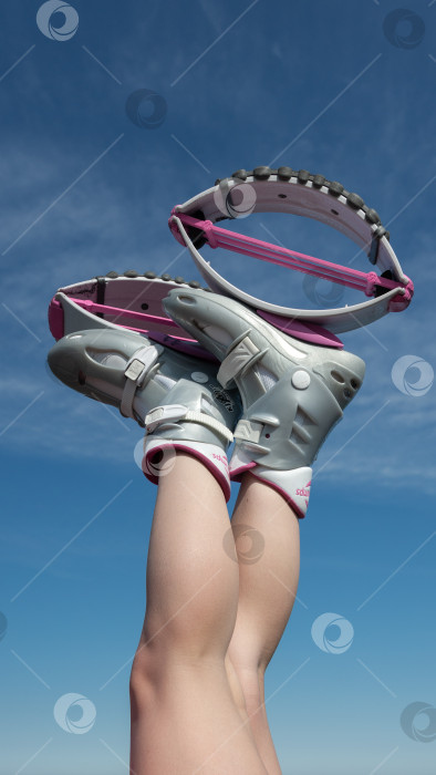 Скачать Женщина, задравшая скрещенные ноги в воздух, обутая в розовые ботинки Kangoo Jumps, во время занятий фитнесом на открытом воздухе на фоне голубого неба солнечным летним днем фотосток Ozero