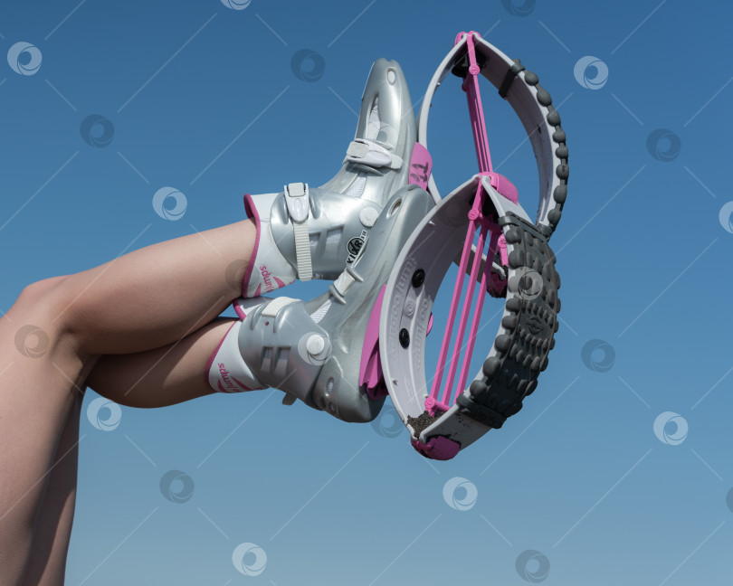 Скачать Обрезанный крупным планом снимок женских скрещенных ног в воздухе, обутых в спортивные ботинки Kangoo Jumps, во время тренировки по фитнесу на открытом воздухе на фоне голубого неба солнечным летним днем фотосток Ozero