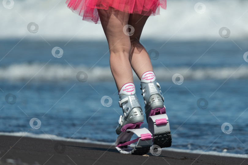 Скачать Укороченный вид сзади на ноги спортивной женщины в спортивных ботинках Kangoo Jumps и короткой юбке, прыгающей и бегущей по пляжу во время аэробной тренировки на открытом воздухе фотосток Ozero