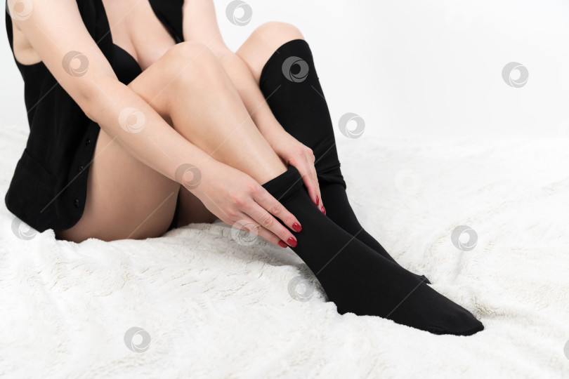 Скачать Обрезанный снимок женщины, тщательно натягивающей на ноги черные колготки. Неузнаваемая женщина на кровати фотосток Ozero