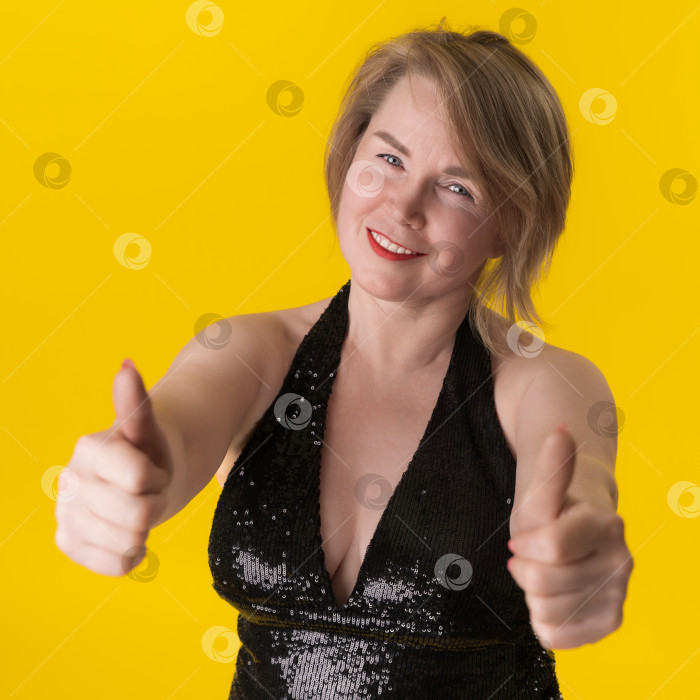 Скачать Портрет пышной зрелой блондинки в вечернем платье, показывающей два больших пальца вверх и удовлетворенно улыбающейся фотосток Ozero