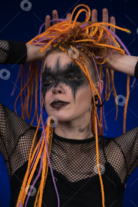 Скачать Молодая женщина с прической из косичек оранжевого цвета и креативным черным сценическим макияжем ужасов, нанесенным на лицо фотосток Ozero