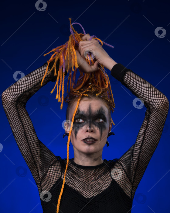 Скачать Неформальная молодая женщина с цветной прической в виде косичек и жутким черным сценическим макияжем, нанесенным на лицо фотосток Ozero