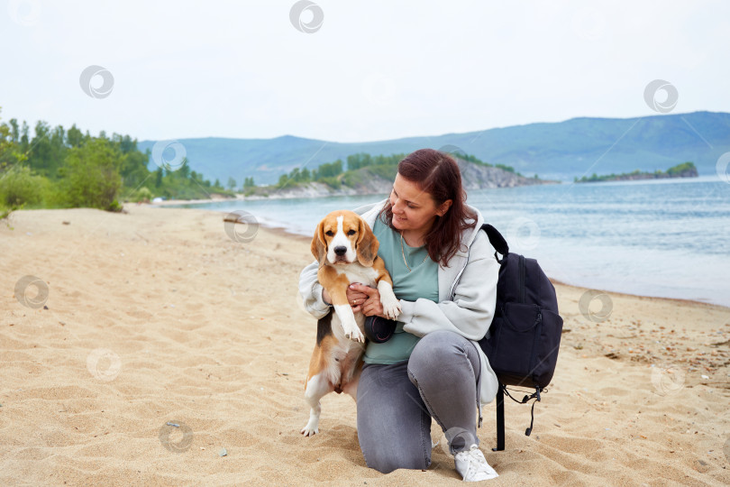 Скачать Женщина-путешественница сидит на песчаном пляже в обнимку со своей собакой фотосток Ozero