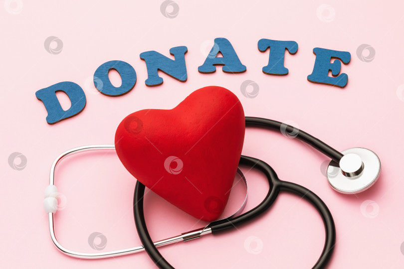 Скачать Слово из деревянных букв, игрушечное сердечко и медицинский стетоскоп на розовом фоне, концепция на тему пожертвования на лечение фотосток Ozero