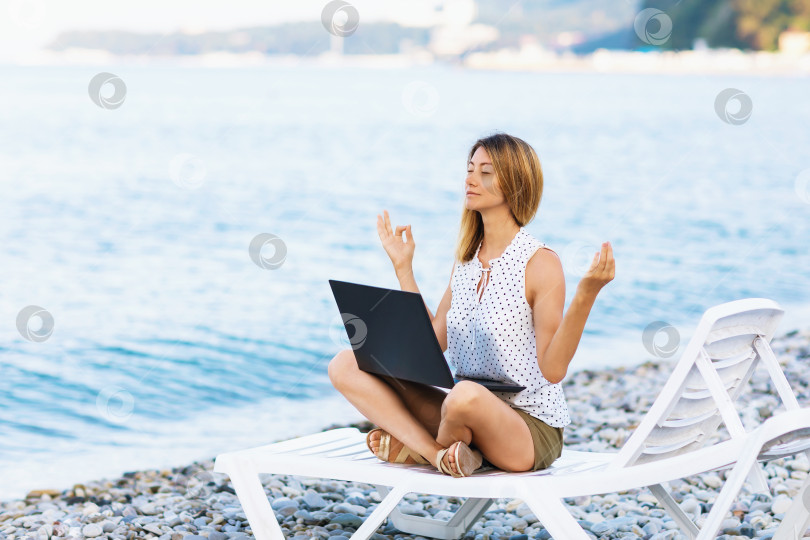 Скачать Спокойная женщина сидит на шезлонге у моря, отвлекается от работы за компьютером, медитирует и снимает негативные эмоции, совмещает удаленную работу с отдыхом фотосток Ozero