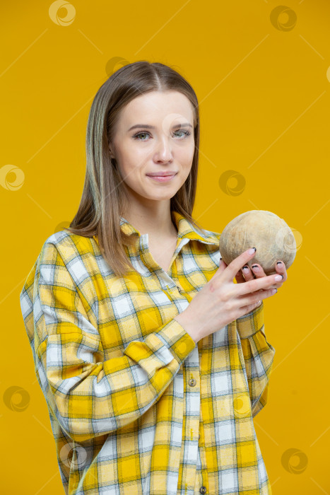 Скачать Снимок симпатичной молодой улыбающейся женщины, смотрящей в камеру, держащей в обеих руках кокосовый орех, изолированный на желтом фоне. Концепция здорового образа жизни, правильное питание, диета, веган, вегетарианец фотосток Ozero