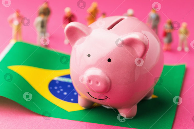 Скачать Копилка, бразильский флаг и пластмассовые игрушечные человечки на цветном фоне, концепт на тему доходов населения Бразилии фотосток Ozero