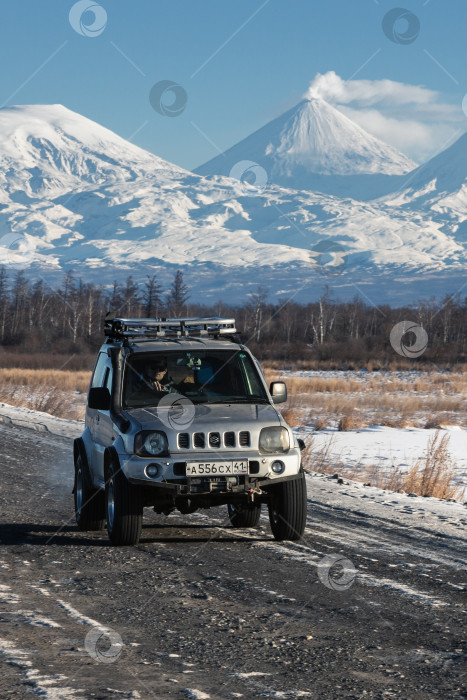 Скачать Японский внедорожник Suzuki Jimny едет по дороге на фоне красивого зимнего пейзажа туристические направления - действующий вулкан Ключевская сопка фотосток Ozero