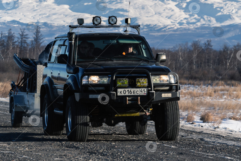 Скачать Японский спортивный внедорожник Toyota Land Cruiser с прицепом, который везет снегоход, едет по дороге на фоне зимнего пейзажа фотосток Ozero