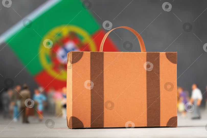 Скачать Картонный чемодан, пластмассовые игрушечные человечки и флаг на абстрактном фоне, концепция на тему переезда или иммиграции в Португалию фотосток Ozero