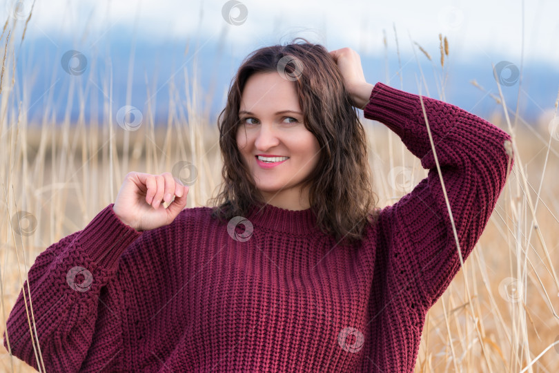 Скачать Портрет симпатичной молодой женщины в коричневом свитере стоит в сухой траве в поле фотосток Ozero