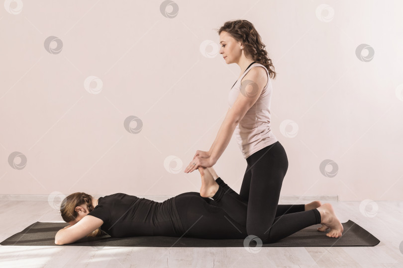 Скачать Учитель йоги помогает ученику размять ноги в студии, прислонившись к стене фотосток Ozero