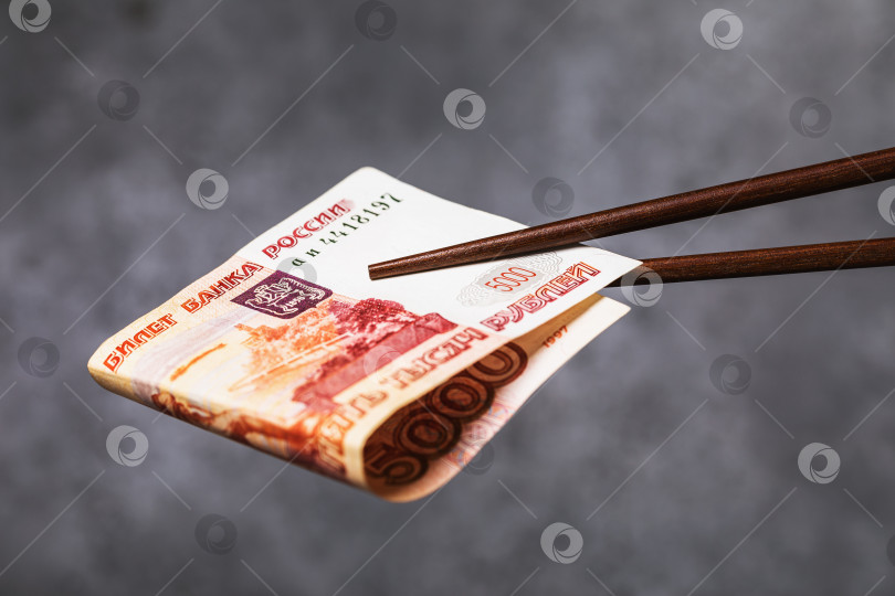Скачать Китайские палочки держат свернутые в трубочку пять тысяч рублей, крупным планом. Концепция отношений между Россией и Китаем фотосток Ozero