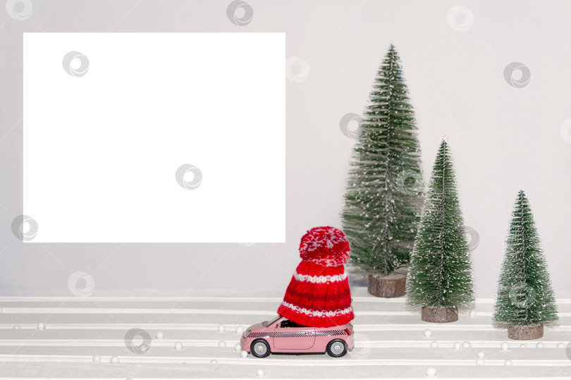 Скачать Счастливого Рождества и Нового года, зимняя иллюстрация. Игрушечный автомобиль в зимней шапке проезжает мимо рождественских елок. Минималистичный дизайн. Макет. фотосток Ozero