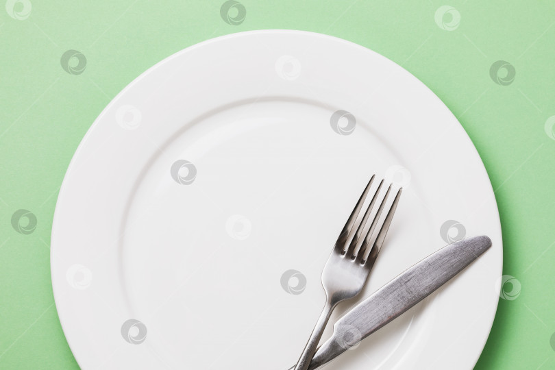 Скачать Пустая белая тарелка и столовые приборы на зеленом фоне, вид сверху фотосток Ozero