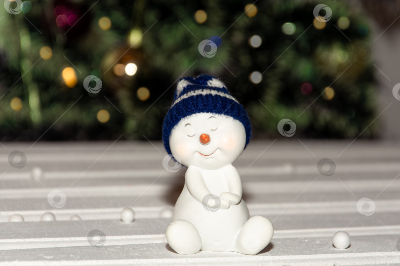Скачать игрушечный снеговик в синей шапочке на фоне рождественской елки. фотосток Ozero