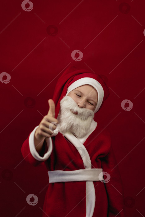 Скачать Мальчик в костюме Санта-Клауса поднимает большие пальцы вверх. фотосток Ozero