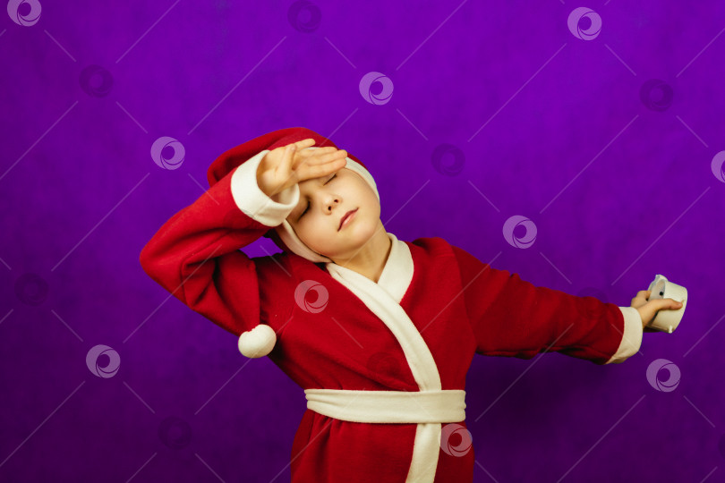 Скачать мальчик в костюме Санта-Клауса прижимает к уху белый будильник. фотосток Ozero