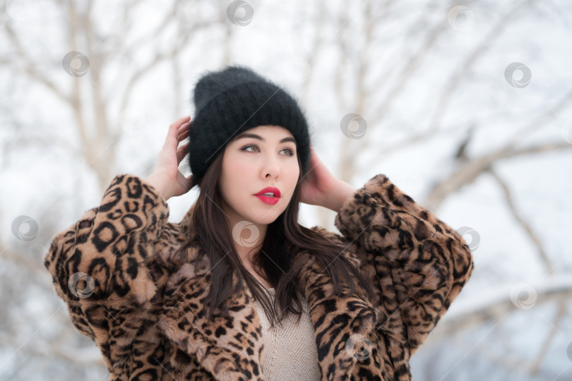 Скачать Зимний портрет женщины с длинными волосами и красными губами в меховой шубе с леопардовым рисунком и черной шляпе фотосток Ozero