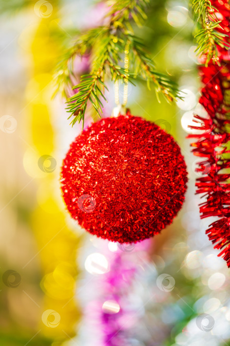 Скачать Красивый красный рождественский шар и блестящая мишура, висящие на ветке дерева. Выборочный фокус на переднем плане, красочное размытое боке на заднем плане фотосток Ozero