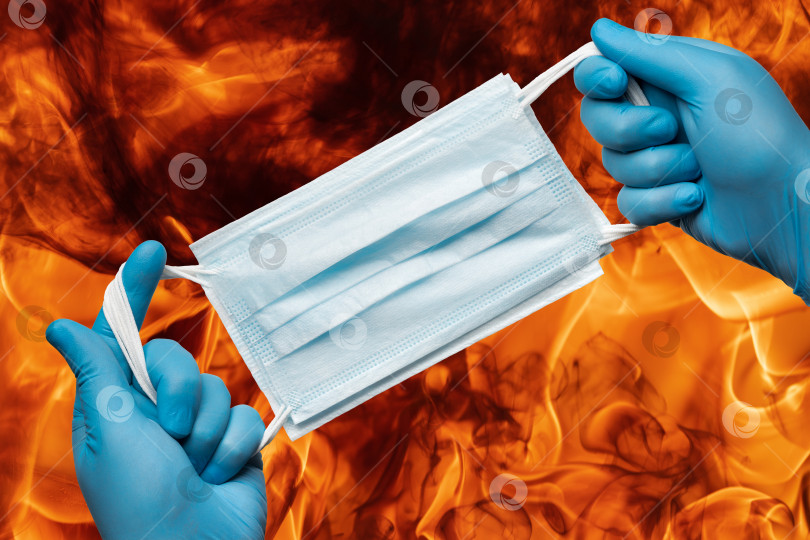 Скачать Фельдшер держит в руках множество медицинских масок для лица в синих перчатках на фоне пламени красного пожара фотосток Ozero