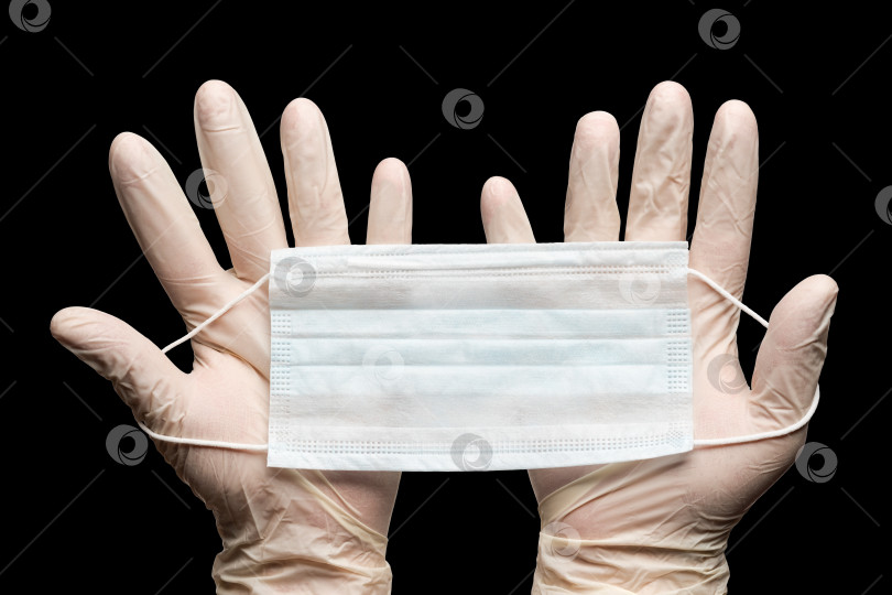 Скачать Врач держит медицинскую маску для лица двумя руками в белых перчатках, выделенных на черном фоне. Концепция карантина по коронавирусу фотосток Ozero